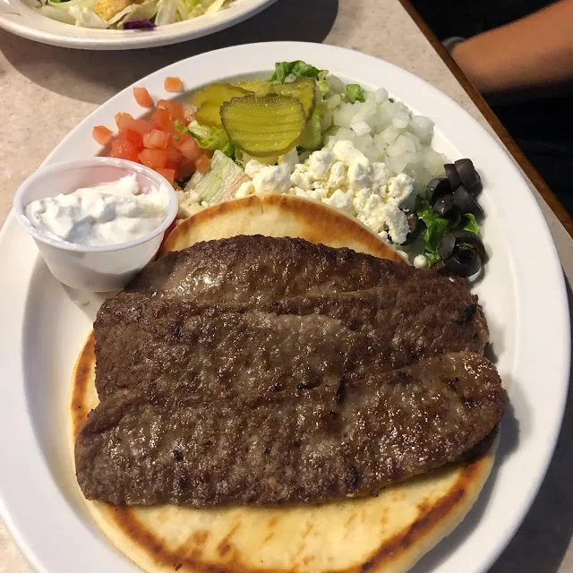Gyro plate with seasoned meat on pita, feta, olives, tomato, onion and tzatziki